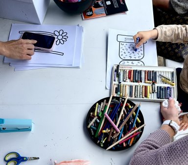 Dzieci biorą udział w warsztatach plastycznych, kolorując przygotowane karty przy stole pełnym kredek, pasteli i materiałów plastycznych.
