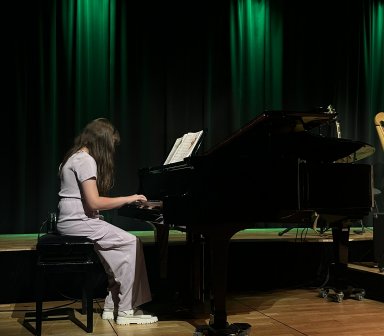 Dziewczynka siedzi przy fortepianie na scenie Fortu Borek i gra utwór z nut ustawionych na pulpicie. W tle widoczne są ciemne kurtyny oświetlone zielonym światłem.