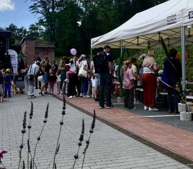 Uczestnicy pikniku ustawili się w kolejce do namiotu z atrakcjami i warsztatami. W tle widoczne są zabytkowe ceglane mury Fortu Borek oraz teren wydarzenia.
